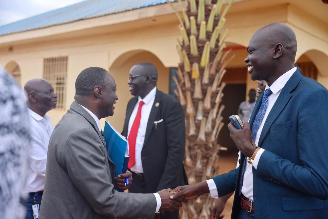 Dr. Gassama shaking hands with a Warrap State official in a warm greeting outside government offices